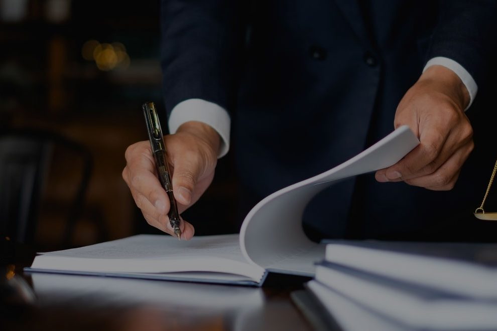 Lista potrzebnych dokumentów Zdjęcie przedstawiające proces podpisywania dokumentów notarialnych przez mężczyznę w granatowym garniturze i białej koszuli, trzymającego czarne pióro.